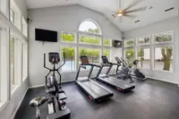 Modern fitness center with large windows offering plenty of natural light, featuring treadmills, an elliptical, and an exercise bike.