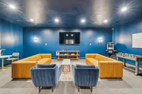 Chic entertainment room with vibrant blue walls, plush mustard sofas, a wall-mounted TV, and a sleek foosball table for ultimate relaxation and fun.