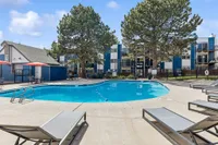 Inviting apartment complex with a sparkling outdoor pool, surrounded by lounge chairs, tall trees, and modern buildings with balconies.