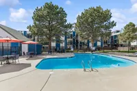Inviting outdoor swimming pool area with vibrant red umbrellas and lush trees, perfect for relaxation in a modern apartment complex.