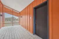 Vibrant and modern entryway with bold orange accents, wood flooring, and a sleek black door, inviting and stylish.