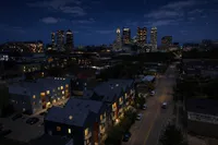 Charming cityscape view featuring modern townhouses with warm lighting, set against a stunning illuminated skyline under a starry night sky.