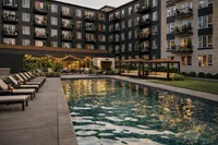 Elegant apartment complex featuring a sparkling outdoor pool, lush greenery, and cozy lounge areas with ambient lighting.