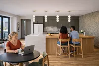 Modern kitchen and dining area featuring elegant pendant lighting, a marble island with wooden accents, and people enjoying the stylish space.