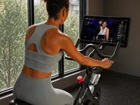 Motivated woman enjoying a high-energy cycling workout on a Peloton bike, engaging with an interactive screen in a bright, modern fitness space.