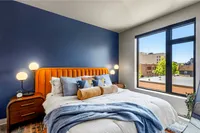 Bright bedroom featuring a plush orange headboard, modern lighting, and a large window with city views.