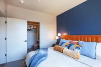 Bright and inviting bedroom with a plush orange headboard, cozy pillows, and a modern blue accent wall, leading to a spacious walk-in closet.