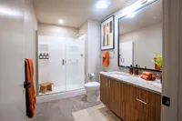 Modern bathroom featuring sleek wood cabinetry, elegant glass shower, and warm orange accents, creating a stylish and inviting space.