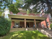 Welcoming brick house with a spacious front porch, surrounded by lush greenery and mature trees.