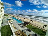 Luxurious beachfront view from apartment showcasing a pristine pool, lush gardens, and serene ocean backdrop with vibrant skies.