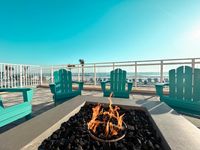 Inviting beachfront patio with turquoise Adirondack chairs around a cozy fire pit, offering panoramic ocean views.