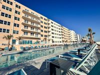 Luxurious apartment complex featuring a modern pool area with sun loungers, surrounded by palm trees and offering a stunning architectural design.