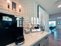 Chic apartment kitchen corner with modern coffee station, elegant lighting, and bright open living space in the background.