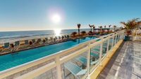 Stunning beachfront apartment view with sunlit pool, ocean waves, and inviting lounge chairs for ultimate relaxation.