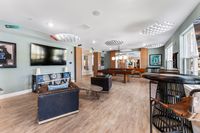Chic modern game room with stylish decor featuring a large TV, comfortable seating, and a pool table under elegant lighting.