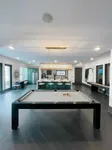 Elegant recreation room featuring a pool table, modern lighting fixture, and open-concept kitchen with bar seating, designed for entertainment and relaxation.
