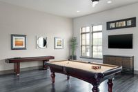 Elegant game room with a pool table, shuffleboard, stylish decor including wall art and a flat-screen TV, providing a perfect entertainment space.