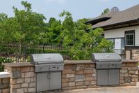 Elegant outdoor grilling area with two modern stainless steel grills and lush green surroundings.