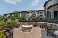 Inviting outdoor patio area with a central fire pit surrounded by Adirondack chairs in front of modern apartment complex.