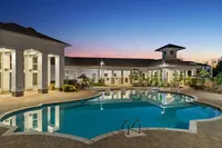 Elegant outdoor pool area with modern architecture at sunset, featuring poolside chairs and beautiful landscaping.