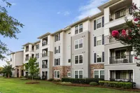 Elegant four-story apartment building with balconies, surrounded by lush greenery and vibrant flowers.