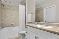 Modern bathroom featuring a sleek countertop, white cabinetry, and a stylish bathtub with marble tile surround.