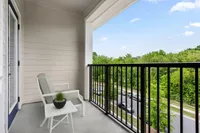 Modern apartment balcony with a comfortable chair and table overlooking lush greenery.