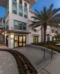 Stylish apartment building exterior with large windows and vibrant palm tree, surrounded by neatly arranged flower beds.