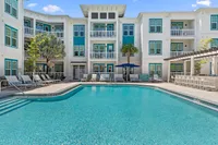 Elegant apartment complex with a sparkling pool, surrounded by palm trees and modern balconies.