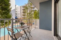 Charming balcony view from a modern apartment overlooking a sunlit swimming pool and lush greenery.