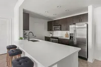 Modern kitchen with sleek dark cabinetry, stainless steel appliances, and a spacious white countertop with stylish bar stools.