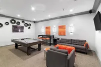 Modern entertainment room featuring a sleek pool table, stylish grey sofas with vibrant orange accents, and contemporary wall art and decor.