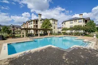 Inviting apartment complex with a refreshing outdoor swimming pool, surrounded by lush greenery and charming architecture.