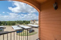 Inviting apartment balcony with a scenic view of manicured greenery and charming residential complexes under a vibrant blue sky.