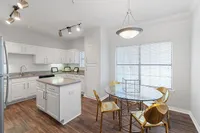 Bright and modern kitchen with elegant white cabinets, sleek island, and chic dining area boasting golden chairs and a glass table.