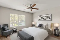 Bright and modern bedroom with elegant decor, featuring a stylish ceiling fan, cozy seating nook by a large window, and tasteful artwork on the wall.