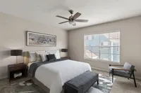 Elegant bedroom with modern decor, featuring a plush bed, sleek lamps, and a cozy seating area. Natural light flows through large windows, creating a serene atmosphere.