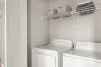 Contemporary laundry room with modern washer and dryer, ample shelving for storage, and neutral decor.