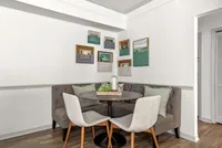 Charming dining nook with a cozy corner bench, stylish round table, and modern chairs, adorned with contemporary art on white walls.