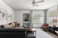 Bright and elegant living room with large windows, contemporary furniture, and tasteful decorative accents. Cozy gray sofa, stylish armchairs, and abstract art create a welcoming ambiance.
