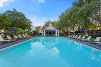 Inviting outdoor pool area with luxurious sun loungers and vibrant umbrellas, surrounded by lush greenery and a charming pool house.
