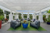 Chic outdoor patio featuring plush seating under a stylish white pergola, surrounded by lush greenery and vibrant potted plants.