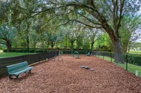 Charming dog park with agility equipment, surrounded by lush greenery and shaded by large trees.