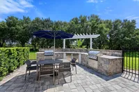 Chic outdoor patio with modern grill and dining area under a stylish pergola, surrounded by lush greenery.