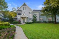 Charming two-story townhouse with elegant facade, surrounded by lush greenery and vibrant flowers under a clear blue sky.
