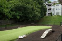 Serene apartment dog park with lush green turf, surrounded by trees and modern building.