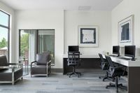 Updated business center with sleek computers, elegant leather chairs, and large windows for natural light.
