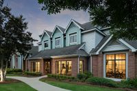 Charming townhouse exterior with brick and pastel siding, featuring large well-lit windows and lush landscaping at sunset.