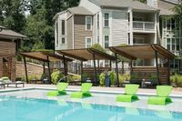 Modern apartment community with a refreshing pool and stylish green lounge chairs under sleek wooden cabanas, surrounded by lush landscaping.