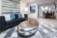 Modern living room with chic black sofa, geometric cushions, and a sleek silver coffee table. Open kitchen and elegant dining area with stylish decor complete the contemporary look.